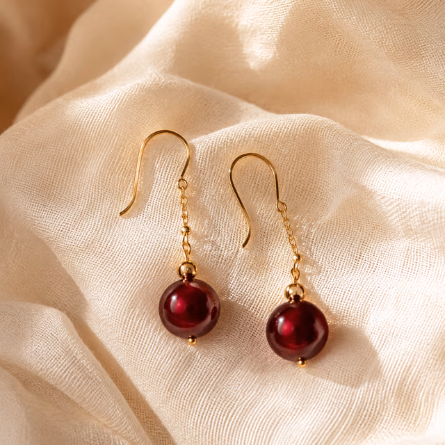 Red wine drop earrings on a gold hook, resting on silk.